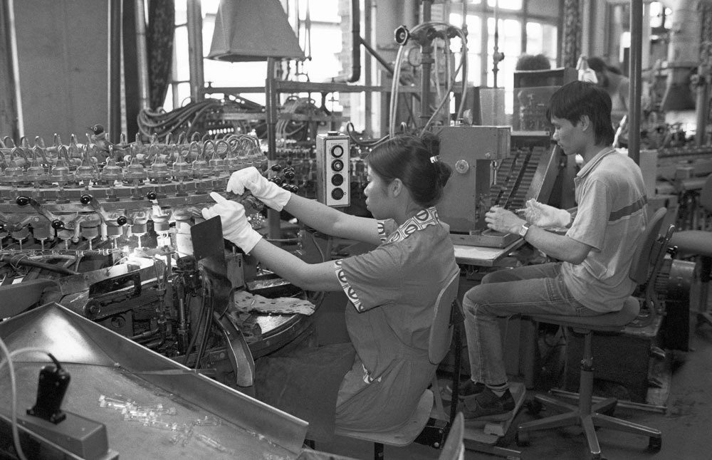 Eine Frau und ein Mann bedienen Maschinen in einer Glühlampenfabrik in Ost-Berlin.