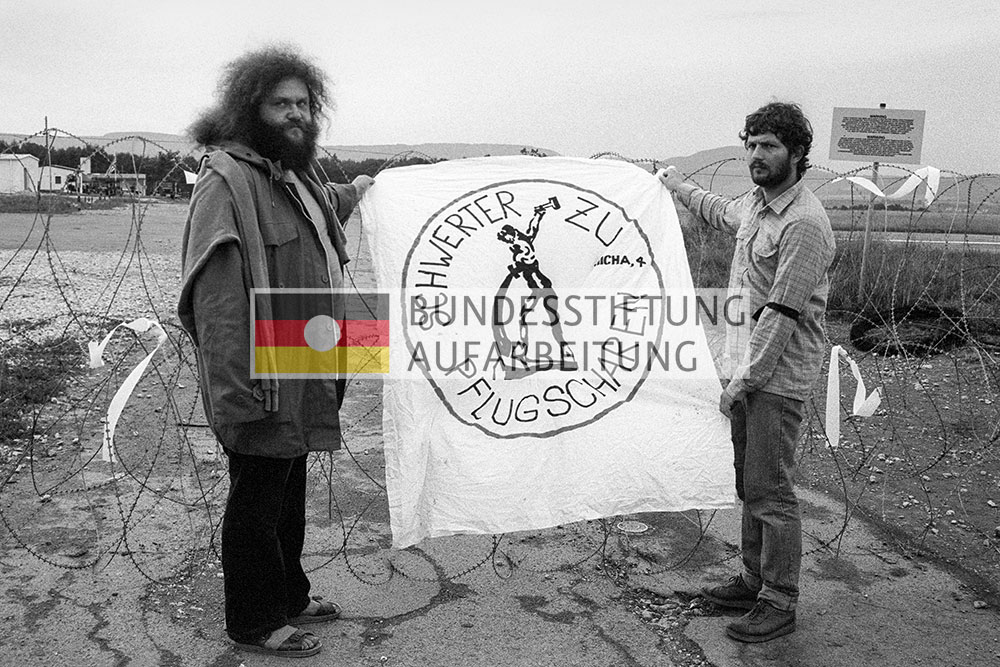 Roesch und Jahn halten ein Transparent mit der Aufschrift "Schwerter zu Pflugscharen" hoch. 
