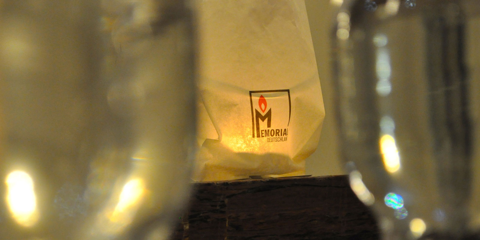Eine Kerze brennt in einer Papiertüte mit den Logo von Memorial darauf