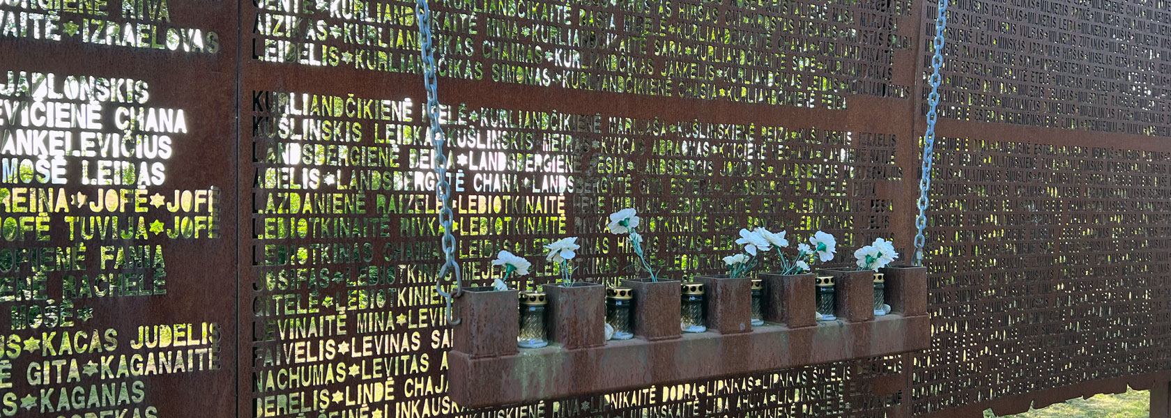 Eine Gedenktafel, vor der Blumen in Behältern aufgehängt sind