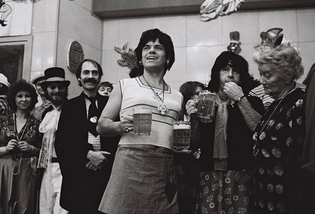 Ein Mann als Frau verkleidet mit zwei Gläsern Bier in der Hand.