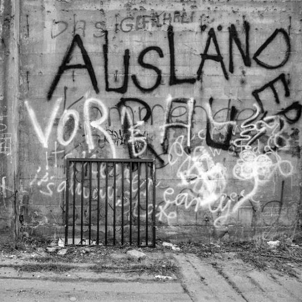 Eine Frau mit Kopftuch läuft an der mit Graffiti besprühten Berliner Mauer entlang. Ein Graffito lautet: Ausländer raus. 