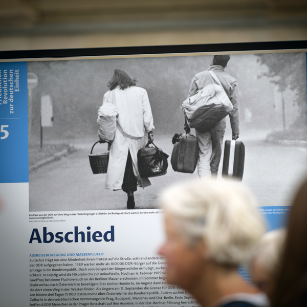 Mehrere Personen schauen sich das Plakat "Abschied" der Ausstellung von der Friedlichen Revolution zur deutschen Einheit an