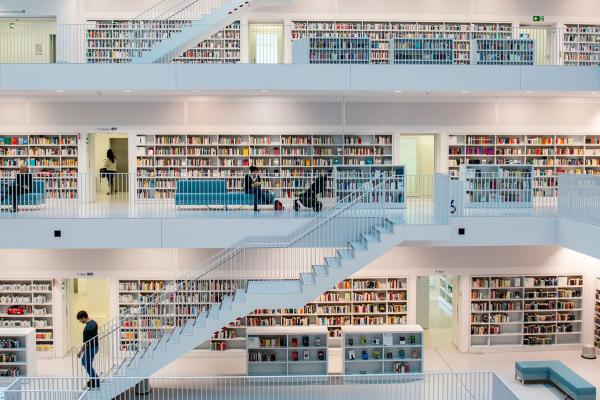 Eine Bibliothek mit vielen hellen Regalen und Treppen, die auf mehrere Etagen führen