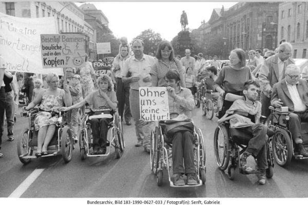 Rollstuhlfahrerinnen und Rollstuhlfahrer mit Plakaten bei einer Demonstration