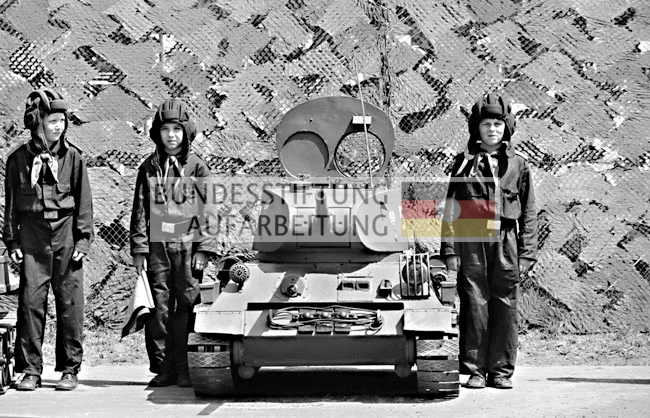 Unter dem Motto " Wir schützen unser sozialistisches Vaterland" werden schon Kinder mit Waffen vertraut gemacht. Bei der Veranstaltung im Friedrichshain sind Minipanzer auf der Basis des Trabant  Autos zu sehen. 